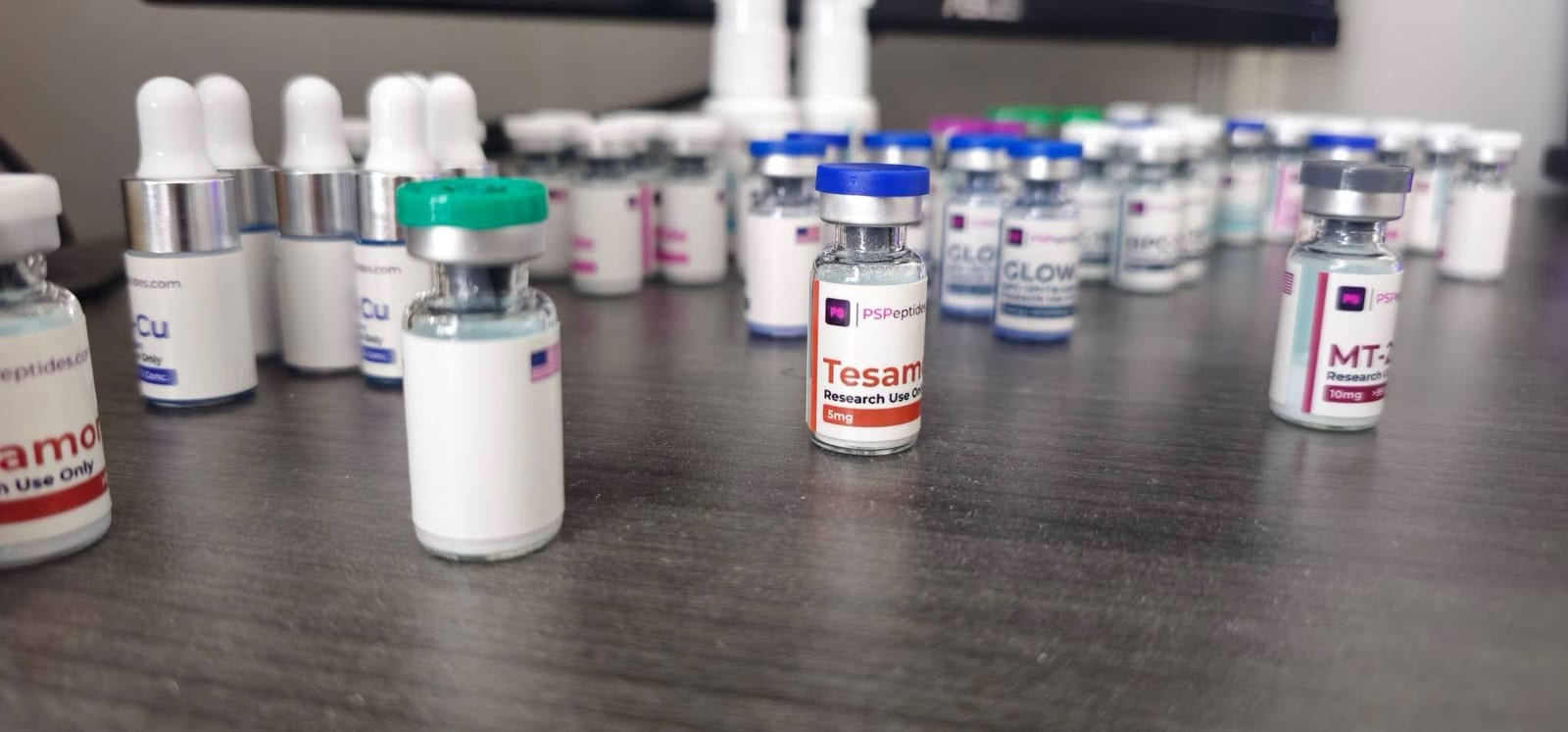 PSPeptides research vials on a desk, including Tesamorelin 5mg, MT-2 10mg and GLOW, each with the store’s purple PS label